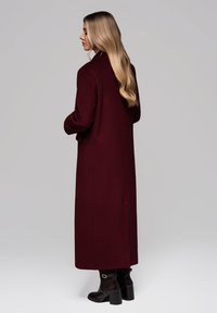 Abrigo largo burdeos de lana, con corte recto y cuello. Combinado con botas de tobillo negras y un acento texturizado.