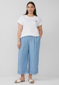 Witte katoenen T-shirt met korte mouwen en een klein geborduurd ontwerp. Lichtblauwe, losse broek met een elastische tailleband. Witte sandalen.