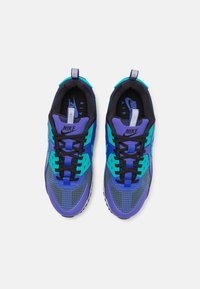 Nike Air-sneakers med en blandning av lila, svart och teal-färger. Nät- och syntetmaterial med rutmönster och kontrasterande detaljer.