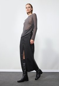 Gray sheer long-sleeve top with a gathered detail, paired with a long black leather skirt featuring a side slit, complemented by knee-high black boots.