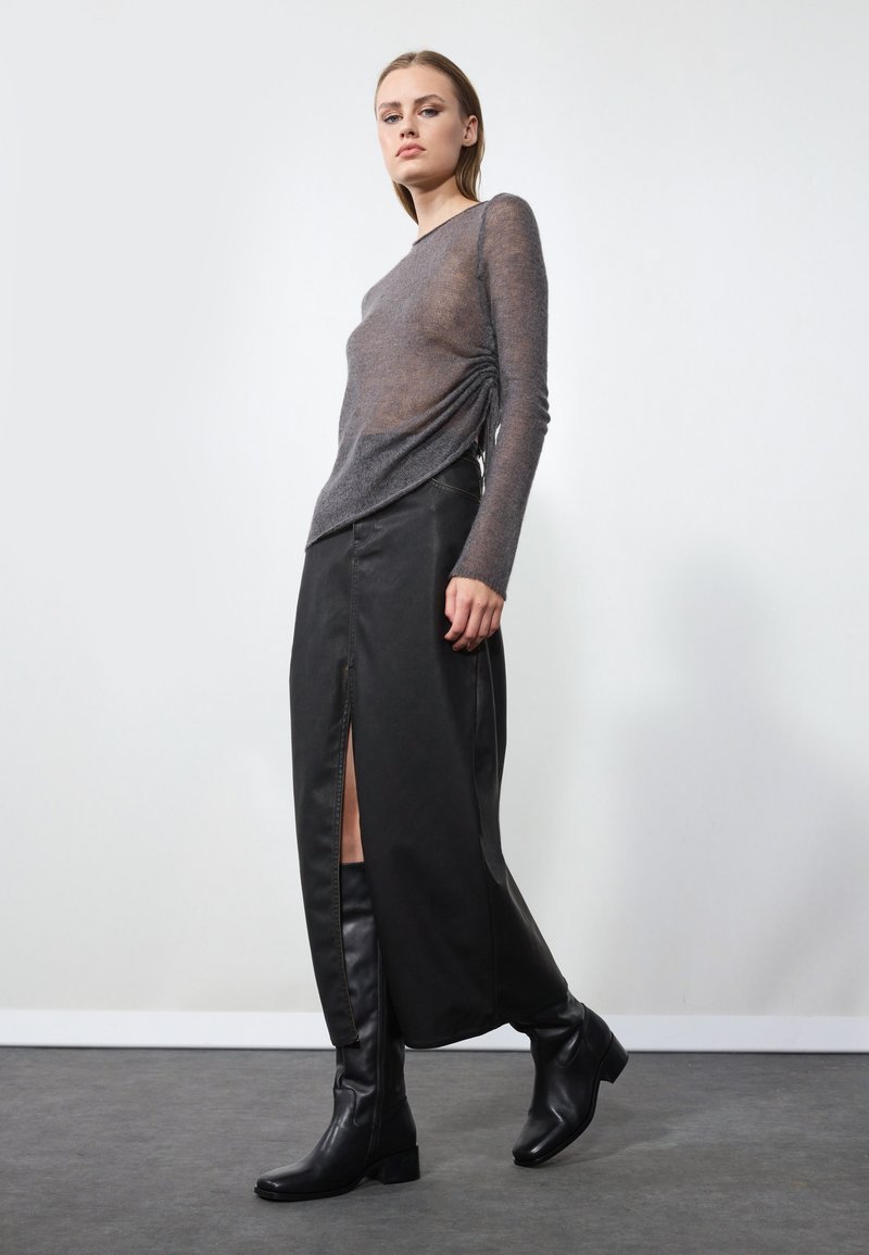 Gray sheer long-sleeve top with a gathered detail, paired with a long black leather skirt featuring a side slit, complemented by knee-high black boots.