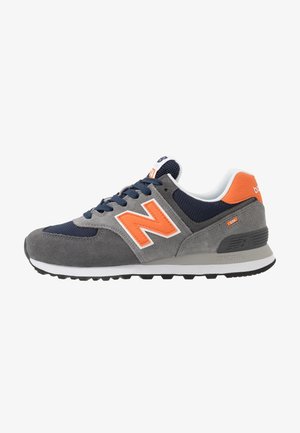 Grijze en marineblauwe sneaker met oranje "N" logo, witte zool en zwarte loopzool, gezien vanaf de buitenkant.