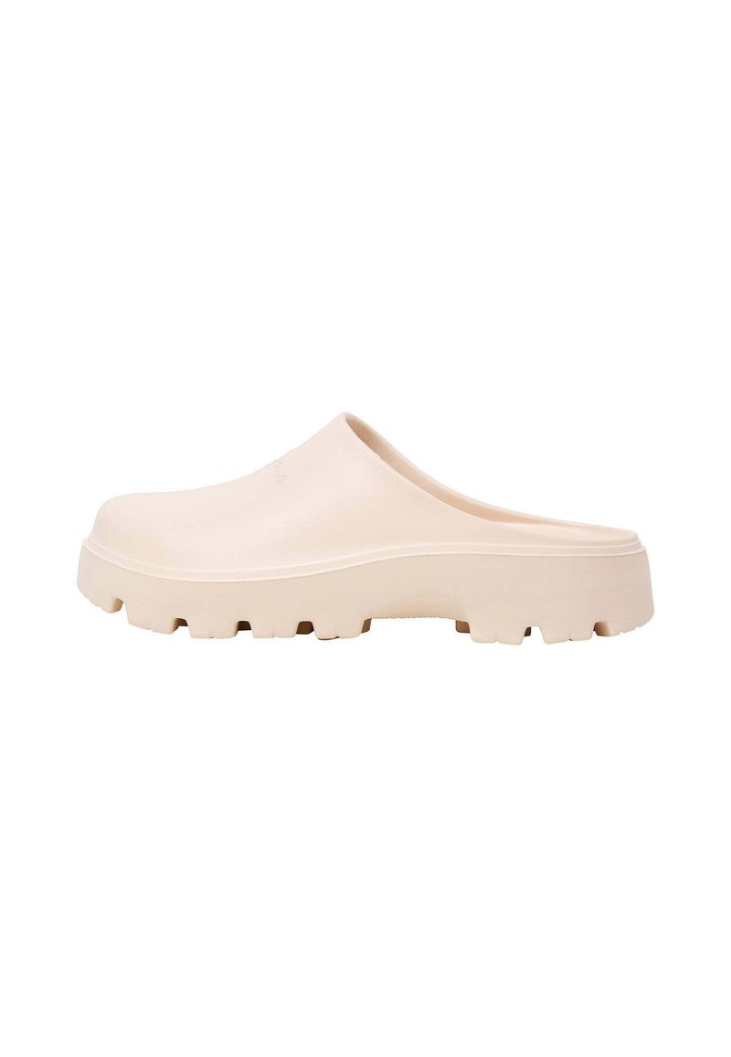 Ljust beige träskor med en slät yta, rundad form och tjocka, strukturerade sulor med framträdande spår för grepp.