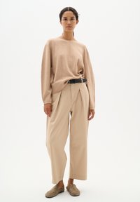 Beżowy sweter dzianinowy z okrągłym dekoltem, zestawiony z jasnobeżowymi spodniami o wysokim stanie i czarnym paskiem. Casulowe buty typu slip-on.