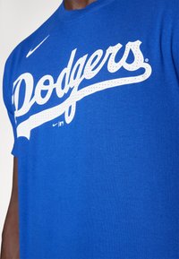 T-shirt in cotone blu con grande logo bianco in corsivo "Dodgers" decorato con accenti a pois. Logo Nike visibile vicino all'orlo.