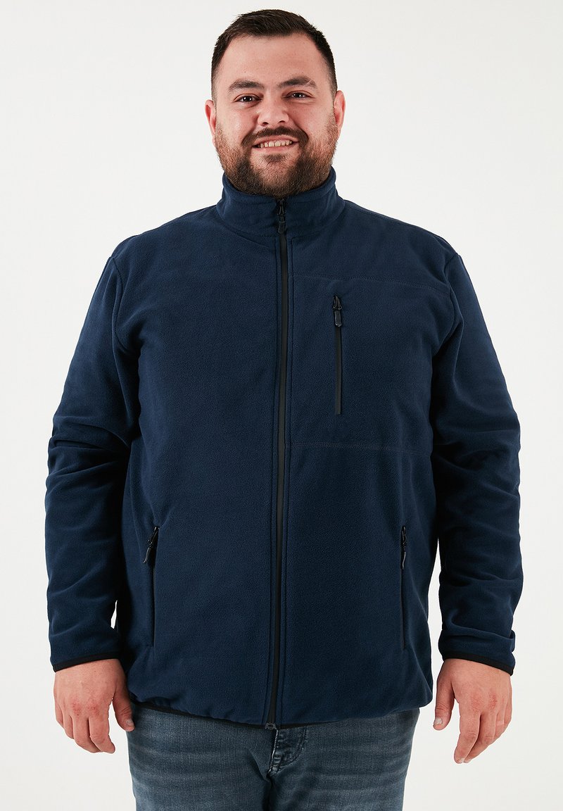 Jūrininkų fliso striukė su aukštu apykakle, priekyje užtrauktuku ir užtrauktukais kišenėse. Pasižymi lygiu paviršiumi ir prigludusiu dizainu.