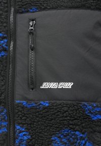 Fekete bolyhos dzseki kék absztrakt mintákkal, cipzáras fekete anyagú zsebbel és fehér "SANTA CRUZ" felirattal. Texturált felület.