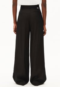 Schwarze, weit geschnittene Hose aus glattem Stoff mit tailliertem Bund und einer einzelnen Gesäßtasche. Verfügt über ein kleines Markenlabel auf der Rückseite.