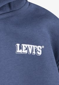 Temno modra kapuca z mehkimi teksturami in velikim belim logotipom "LEVI'S" spredaj. Klasična zasnova s kapuco na vrvico.