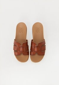 Brune lærslidesandaler med åpen tå, med en løkke- og utklippsdesign på stroppen. Myk skuminnersåle for komfort.