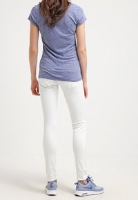 Camiseta de manga corta ajustada azul con tejido texturizado, combinada con pantalones vaqueros skinny blancos y zapatillas deportivas azul claro con detalle de cordones.