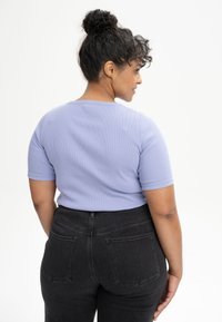 Fijn fitting lavendelkleurig ribbelshirt met korte mouwen, gecombineerd met hooggerite zwarte denim jeans met achterzakken.