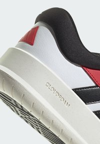 Sneaker bianco e nero con accenti rossi, sopracolo in tessuto morbido, suola in gomma e "CLOUDFOAM" impresso sul tallone. Forma arrotondata.