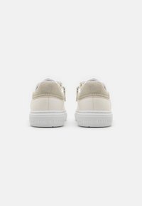 Białe sneakersy z gładką skórzaną cholewką i teksturowanym beżowym akcentem na pięcie. Logo wytłoczone na białej gumowej podeszwie.