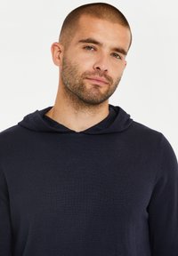 Marineblaue Kapuzenjacke aus strukturiertem Strickstoff, mit einer Kordelzugkapuze und einer lockeren Passform. Minimalistisches Design, keine sichtbaren Muster oder Akzente.