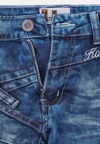 Jeans in denim blu scuro con chiusura a zip, bottone metallico e cuciture arancioni. Presentano un logo ricamato e più tasche.