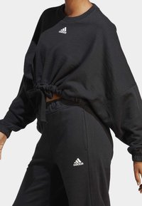 Svart avkortad sweatshirt med dragsko och ribbade muddar, matchad med svettbyxor som har en Adidas-logga på höften.