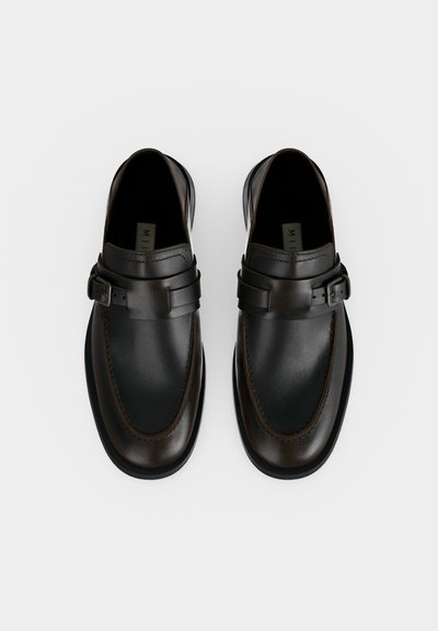 Paire de mocassins en cuir marron foncé sans lacets avec détail boucle sur fond blanc, vue de dessus.