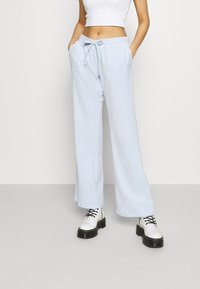 Pantalones de chándal de pierna ancha en azul claro, hechos de tela suave, con una cintura elástica y cordón, combinados con botas blancas de cordones.