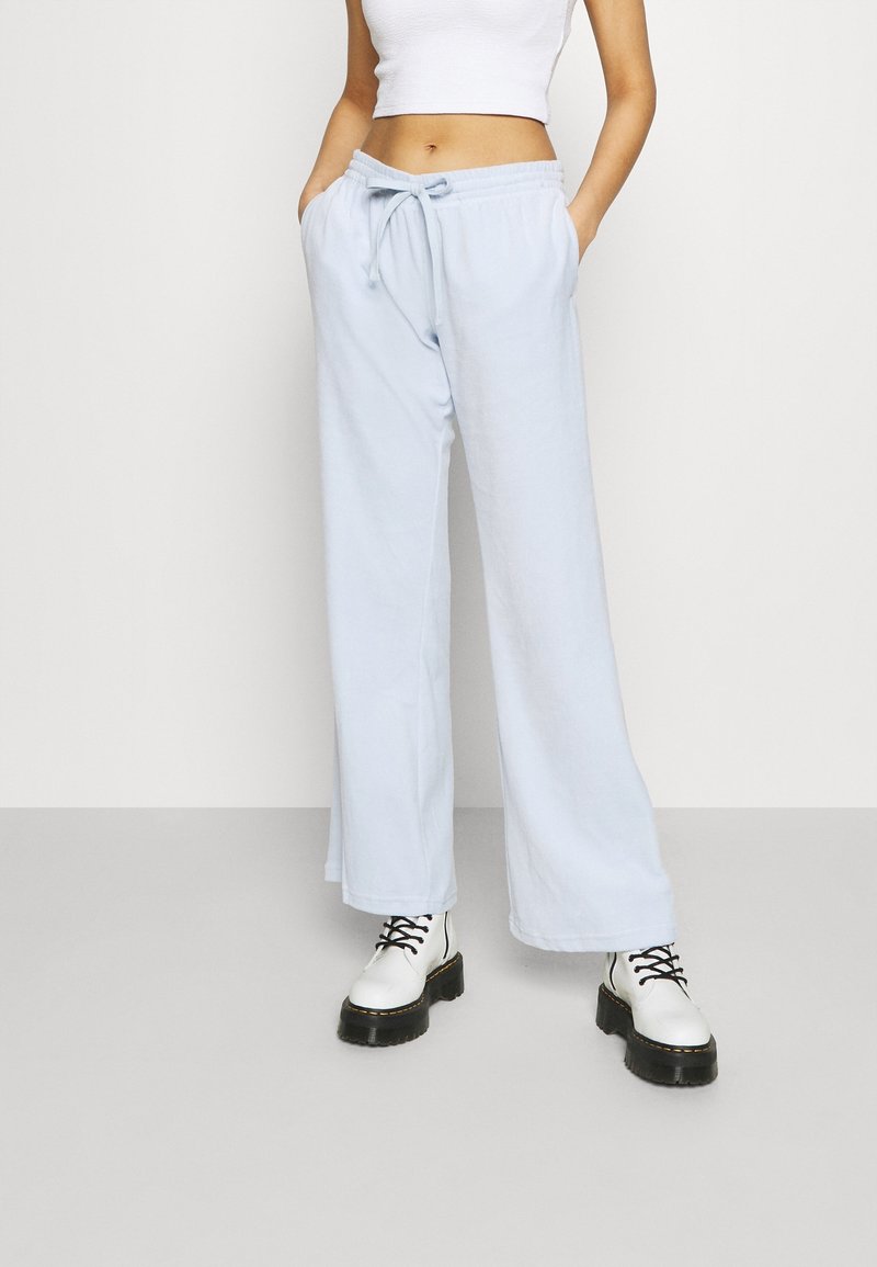 Pantalones de chándal de pierna ancha en azul claro, hechos de tela suave, con una cintura elástica y cordón, combinados con botas blancas de cordones.