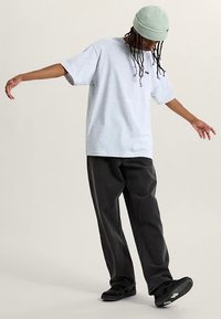 Lysegrå oversized t-shirt med korte ærmer, kombineret med sorte, rummelige bukser og en lysegrøn ribstrikket hue. Sorte sko fuldender looket.