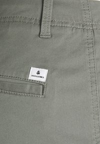 Šedé bavlněné kalhoty s zadní kapsou a bílou nášivkou JACK & JONES, výraznými švy a hladkým povrchem.