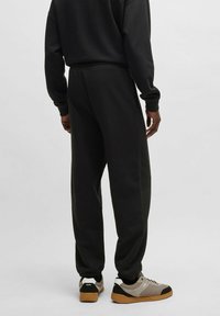 Sorte sweatpants med elastiske manchetter og snøre i taljen, parret med grå og sorte sneakers med tekstureret design og logo.