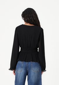 Must mustriga mustriga, millel on pikad varrukad ja kokkusurutud vöökoht, kombineeritud kõrge vöökohtavöödega sinistest denim pükstest. Lihtne kaelus ja voolav kangas.