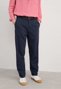 Marineblauwe chinos met een relaxte pasvorm, gemaakt van katoen, voorzien van voorzakken en een riem. Gecombineerd met witte sneakers en een roze shirt.