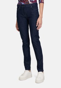 Jeans skinny in denim blu scuro, con un classico design a cinque tasche, dettagli cuciti e abbinati a sneaker bianche.