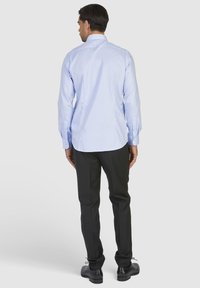 Blauw overhemd met lange mouwen, tailored fit, met een rugpand en plooien. Gecombineerd met zwarte broek en zwarte schoenen.