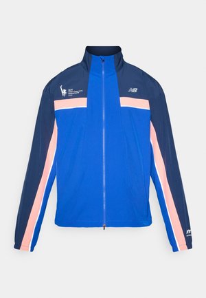 Modrá bunda s námořnickými a růžovými pruhy, vysoký límec, zapínání na zip a sportovní logo na levé hrudi. Lehký, hladký materiál.