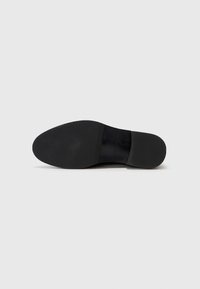 Black leather shoe sole featuring a rounded toe, smooth texture, and minimal tread pattern for traction. Clean design with no accents.