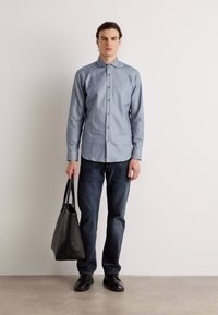 Camicia a righe blu, pantaloni in denim scuro, scarpe nere e una grande borsa tote nera, con una texture liscia e una vestibilità su misura.