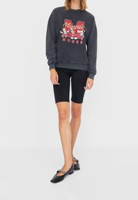 Kolen sweatshirt met "Minnie Mouse" graphic, zwarte fietsbroek en zwarte flats met kettingaccent. Casual outfit, relaxte pasvorm.