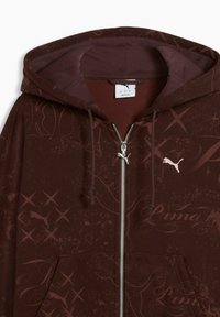 Sweat à capuche zippé Puma marron foncé avec capuche, cordons de serrage, poches avant et imprimé discret sur l'ensemble avec logo Puma et écriture.
