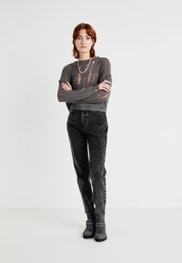 Grijze, gebreide cropped trui met een ribbeltextuur en versleten details, gecombineerd met hooggewaisted, vervaagde zwarte spijkerbroek en grijze enkellaarsjes.