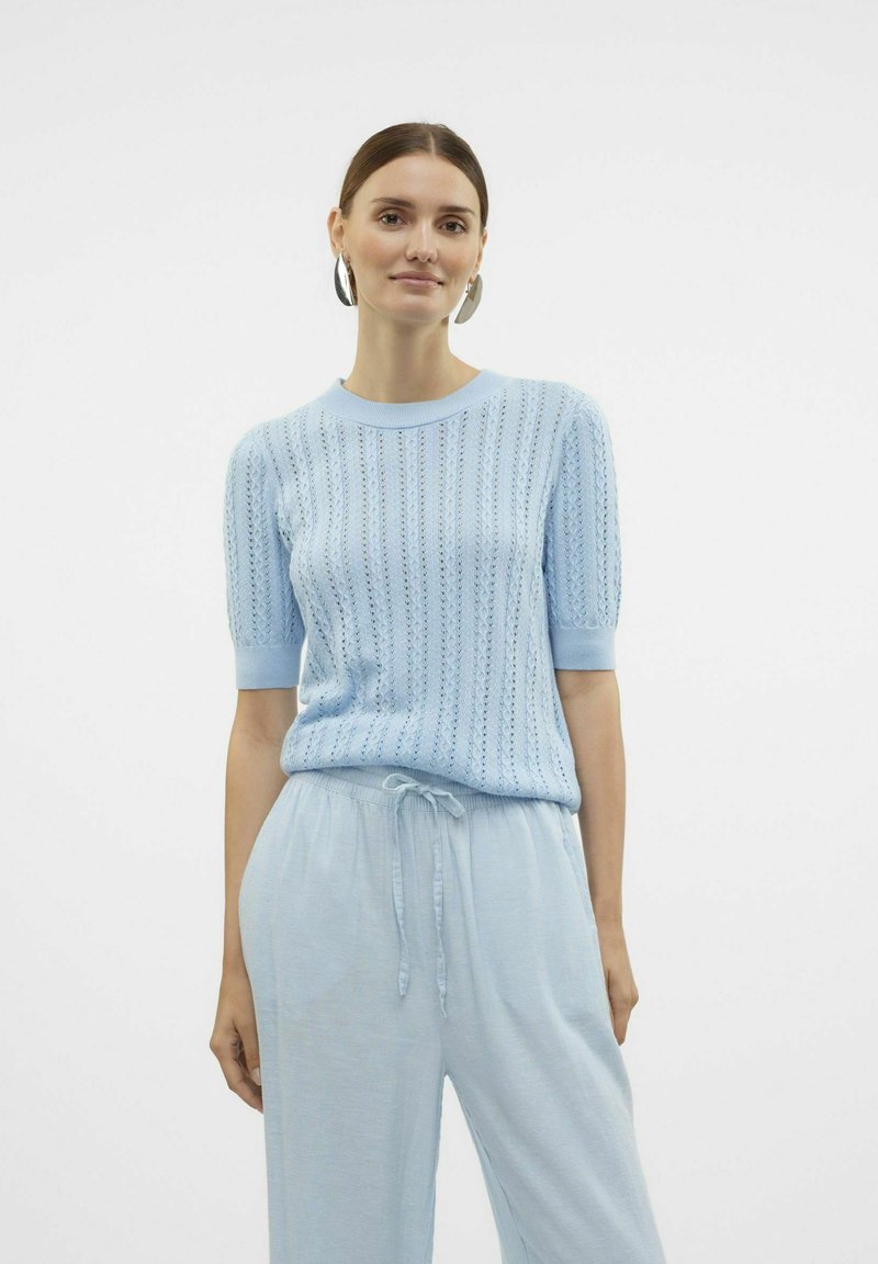 Maglione lavorato a maglia blu chiaro a maniche corte, con un motivo simile a pizzo e colletto a coste. Abbinato a pantaloni blu chiaro coordinati.