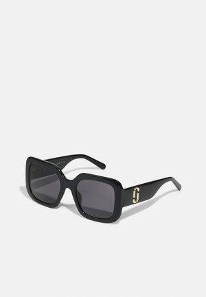Óculos de sol pretos com uma armação quadrada robusta, lentes escuras, acabamento brilhante e um detalhe em dourado nas hastes.