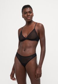 Svart undertøysett laget av gjennomsiktig prikkete mesh. Bh-en har en trekantet fasong med tynne stropper, mens truse har et matchende design.