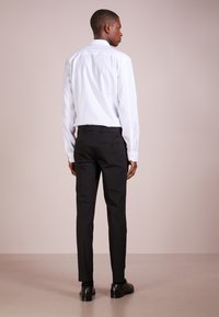 Hvit skjorte med klassisk krage, svarte skreddersydde bukser, glatt stoff og minimalistisk design, kombinert med svarte sko og synlige baklommer.