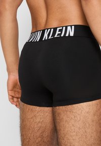 Black cotton boxer briefs with a wide white waistband featuring "CALVIN KLEIN" logo. Smooth texture and fitted design for comfort.