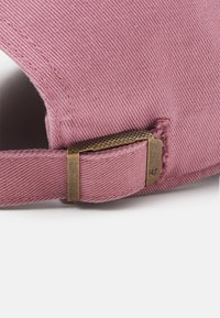 Casquette de baseball en coton rose avec un fermoir en laiton texturé. Le tissu présente un côtelé diagonal distinct, mettant en valeur un bord cousu propre.