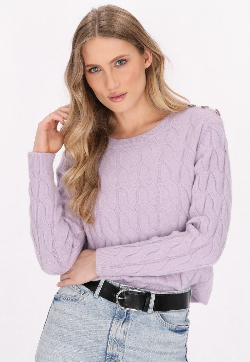Maglione lila a maglia rasata con polsini a coste e scollatura rotonda. Presenta un dettaglio di bottone sulla spalla. Abbinato a jeans a vita alta.