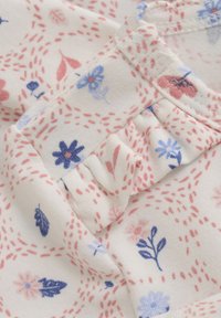 Hvidt stof med et blomsterdesign i blå, pink og rød. Har sammensamlede flæser og stingdetaljer i et gentaget prikket mønster.