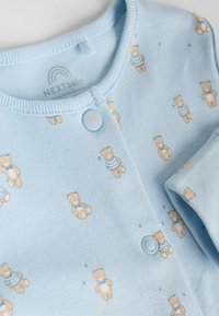 Cardigan pentru bebeluși de culoare albastru deschis, cu imprimeu ursuleț de pluș, prevăzut cu guler rotund, închidere cu nasturi și textură moale din bumbac. Accentuare cu modele mici.