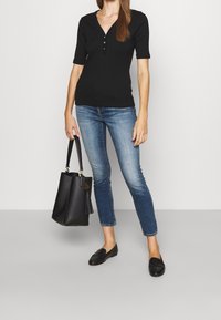 Svart ribbad kortärmad topp med tre knappar, tillsammans med ljusblå figurnära jeans. Svarta läder loafers och en svart fransad tote-väska.