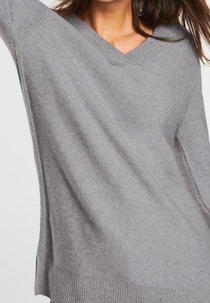 Femme portant un pull à col en V gris clair doux avec manches longues et ourlet et poignets côtelés.