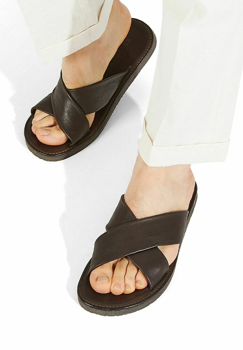 Sandali in pelle marrone con un design a fascetta incrociata e suola piatta. La superficie testurizzata e i dettagli delle cuciture arricchiscono l'aspetto complessivo.