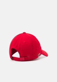 Piros baseball sapka, ívelt karimával, állítható pánttal a hátsó részen, és hímzett logóval az oldalon. Az anyag sima és jól formázott.